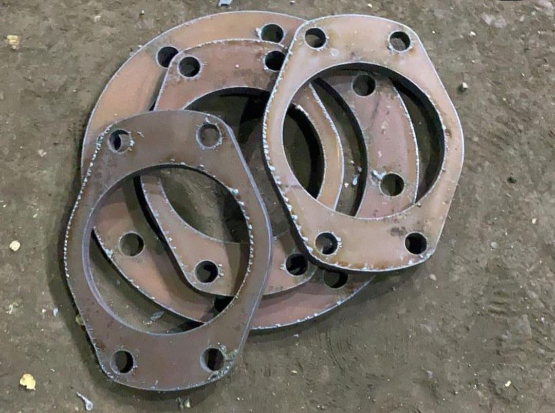 A pile of rusty metal gaskets, each with four holes, lies on a rough, dusty concrete floor. The image conveys an industrial, gritty tone.